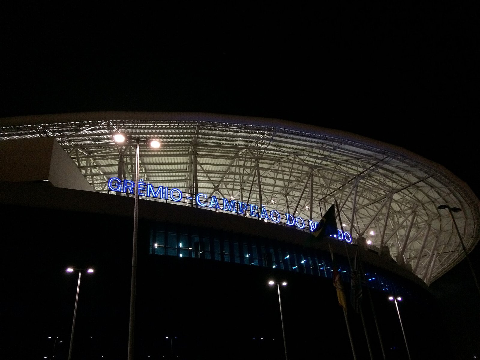 Fachada iluminada e cobertura da Arena do Grêmio, estádio do Grêmio em Porto Alegre, à noite, com o letreiro do estádio